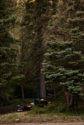 a campsite with a campfire and a guy bent over.
